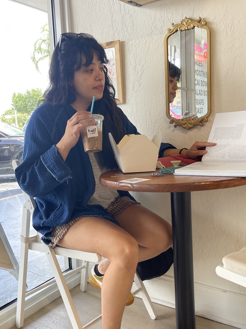 Guest reading with an iced coffee inside Dèlf Café in Sunrise, FL